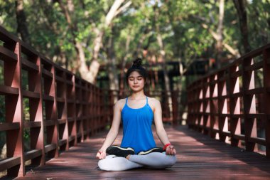 Genç bir kadın ormanda lotus pozisyonunda meditasyon yapıyor.