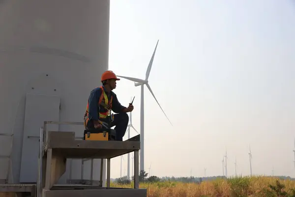 Specialist wind turbine technician working at the base of the turbine. Wind turbine service technician wearing safety uniform and safety harness working at windmill farm