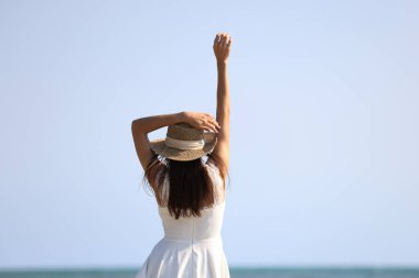Genç ve çekici etnik Tayland milenyum kadını güneşli kollarını yana açarak poz veriyor ve beyaz günlük kıyafetler giymiş çeşitli pozlar okyanusta kumlu sahilde duruyor. Seyahat aşkı