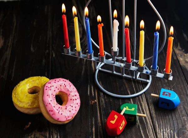 Jewish holiday Hanukkah background. Traditional dish is sweet donuts. Hanukkah table setting candlestick with candles and spinning tops on black background. Letters of Hebrew alphabet on tops. Copy
