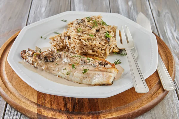 stock image White fish fillet with risotto on plate with fork on wooden background.