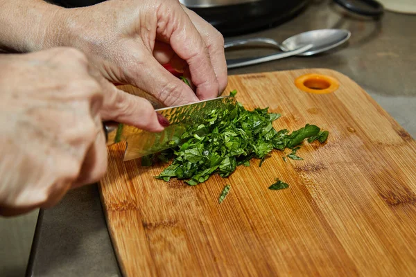 Chef cuts fresh basil leaves on a wooden board for cooking.