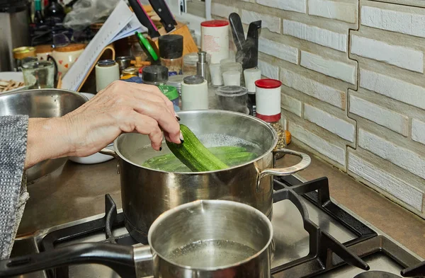 Chef puts zucchini in pot on gas stove in the kitchen.