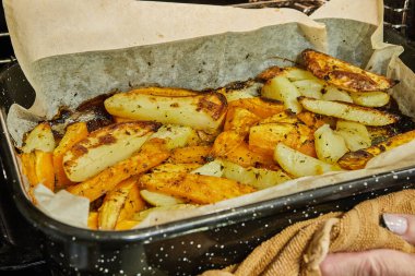 Potatoes with sweet potatoes are baked in the oven on baking sheet.