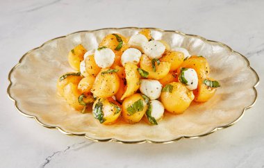 Salad with melon mugs baby mozzarella and herbs on white marble.