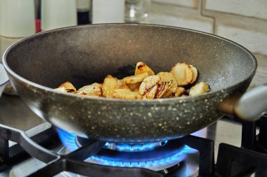 Sliced potatoes are fried in frying pan on gas stove.