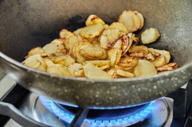 Sliced potatoes are fried in frying pan on gas stove.
