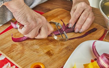Chef cuts slices of Carrots of three colors in the kitchen on wooden board.