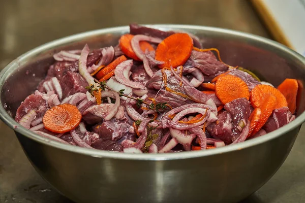 Diced beef with onions and carrots in metal bowl ready for cooking.