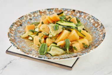 Salad with melon zucchini and herbs on white marble.