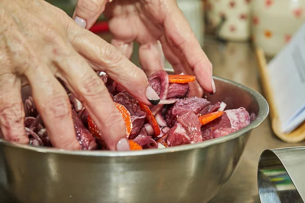 Cook mixes the diced beef meat with onions and carrots in metal bowl.