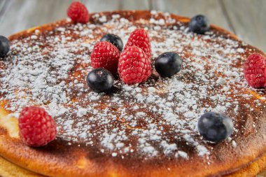 Cheesecake without dough with red fruit syrup and raspberries and blueberries.