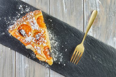 Triangle cake with apricots baked in the oven on wooden background.