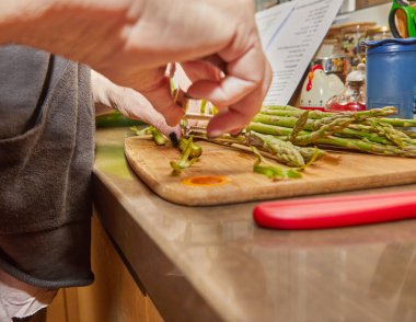 Chef prepares Asparagus in the kitchen on wooden board according to recipe from the Internet.