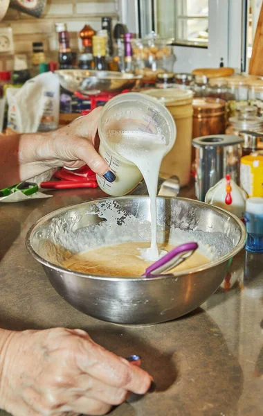 stock image Chef in the home kitchen pours milk from measuring glass into pot with ingredients.