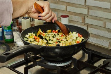 Şef doğranmış domates ve patlıcanla gaz sobası malzemelerini karıştırıyor..