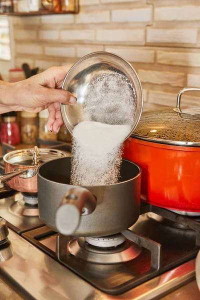 Chef pours sugar into pot on the gas stove.