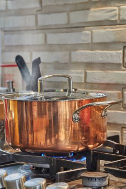 Bulaşık kapaklı bakır tencere, ocakta ateşte pişiyor. Buhar tencerenin üzerinden yükseliyor..
