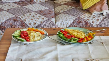 Parmesan peynirli omlet, salatalık, vişneli domates ve kanepenin önündeki sehpanın üzerindeki tatlı biberden oluşan sağlıklı bir kahvaltı..