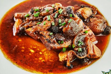 Süslü kırmızı şarap tabağında sarımsaklı ve yeşil soğanlı Ossobuco. Kapat..