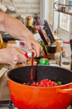 Şef, tüpten tavaya domates ezmesi ve gazlı soba koyuyor..