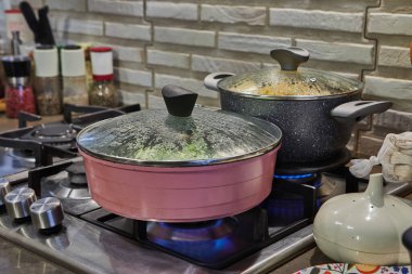 Yakın plan taze kabak dilimleri gaz ocağında tavada cızırdıyor, alevler tabağı yalıyor ve cam kapak tavayı kaplıyor, ağız sulandıran bir yemek sahnesi yaratıyor..