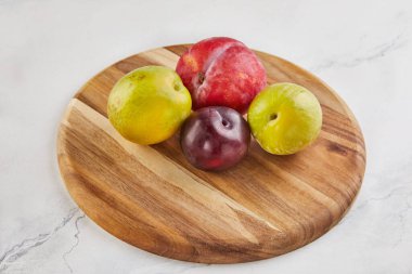 Kırsal ahşap bir tezgahta, temiz ve zarif beyaz mermer arka planda çeşitli taze erikler. Renkli meyveler, doğal ve sağlıklı iyiliklerin cömert bir gösterisini sunar..