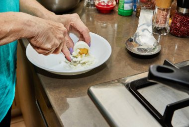 Chef crushes hard-boiled egg on plate with fork.