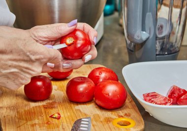 Parlak, modern bir mutfakta ahşap bir kesme tahtasıyla taze domatesleri ustalıkla dilimleyen bir şefin elinin yakın plan çekimi. Yetenekli şef lezzetli bir yemek hazırlamak için keskin bir bıçak kullanıyor..