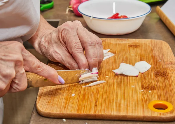 Close-up of a chef\'s hands expertly slicing fresh radishes on a wooden cutting board in a bright modern kitchen. An experienced chef uses a sharp knife to prepare delicious food.
