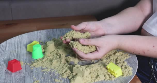 若い女の子はテーブルに座り 運動的な砂で遊び 手を使ってさまざまな形や型を作り出し 彼女の創造性と想像力を表現しています — ストック動画