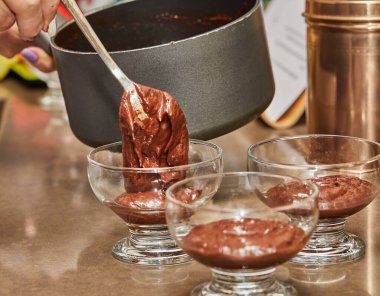 Yetenekli bir şef, sıcak bir ev mutfağında lezzetli bir yığın çikolatalı mus yapıyor. Zengin ve kremalı tatlıları pişirmek için tencere ve kaşık kullanıyor..