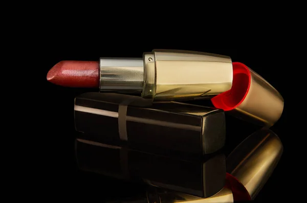 Red and gold metallic lipstick isolated on black background with reflection. Beauty, glamour, fashion, luxury makeup concept. High quality and high resolution image.