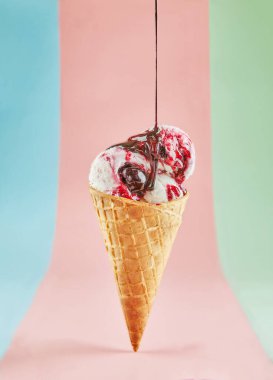 İki kepçe çilekli ve vanilyalı dondurmalı tek bir dondurma külahının yakın plan görüntüsü. Üstüne de çikolata sosu serpiştirilmiş. Pastel pembe arka planda izole edilmiş.. 
