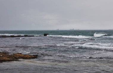 Akdeniz 'deki deniz kıyısının çarpıcı güzelliğinin tadını çıkarın. Hafif yağmur sırasında dalgalar Akdeniz gökyüzünün altındaki rıhtıma çarpıyor ve güzel ve huzurlu bir manzara yaratıyor..