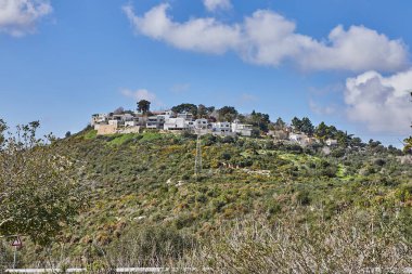 Çağdaş bir villaya giden toprak yolu olan kayalık bir tepe açık mavi gökyüzünün altında kabarık beyaz bulutlarla çevrili yeşil bir villa rahatlama için ideal bir manzara yaratıyor..