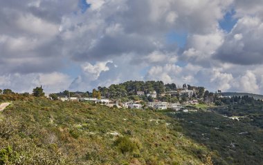 Çağdaş villalara giden toprak yolu olan kayalık bir tepe. Açık mavi gökyüzünün altında, kabarık beyaz bulutlarla çevrili yeşil villalar. Rahatlamak için güzel bir manzara yaratıyor..