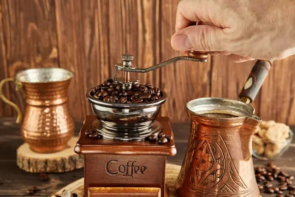 Grinding coffee beans into a vintage coffee grinder, coffee maker and copper cup on a wooden background.