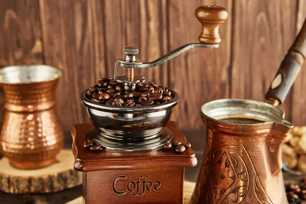 Vintage coffee grinder, cezve for brewing coffee and copper cup on wooden background.