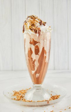 Tabaktaki bardakta bir milkshake 'in yakın çekimi, çeşitli malzemelerle yapılan kremalı içeceği sergiliyor ve içecek kabında servis ediyor.