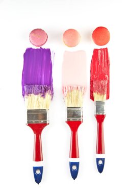 Kırmızı saplı üç boya fırçası, her biri renkli boyaya batırılmış, beyaz arka planda benzer makaronlar var..