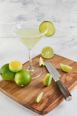 Green and yellow macarons paired with lime wedges and white chocolate, set beside a margarita with a salted rim. clipart