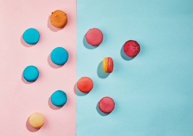 Farklı renkte ve aromalı çok renkli badem kurabiyeleri mavi-pembe arka plana saçılmış..