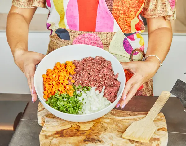 Stock image Close-up of a woman holding a bowl of fresh minced meat, vegetables and herbs in the kitchen.