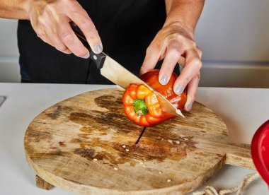 Yakın plan çekimler, ahşap kesme tahtasının üzerinde kırmızı bir dolma biberi dilimleme, yemek hazırlığı ve taze malzemeler..