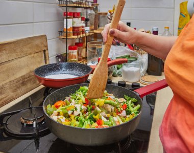 Ev mutfağında rengarenk kızartılmış sebzelerle el çırpma malzemelerini tavaya karıştır..