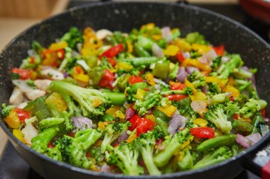 Renkli karıştırılmış sebzeler, tavukla birlikte bir mutfak ortamında gaz ocağında pişiriliyor..