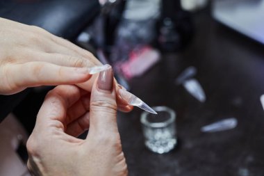 Profesyonel bir kuaförde bir müşterinin parmağına tırnak uzatma uygulayan bir tırnak teknisyeninin yakın çekimi..