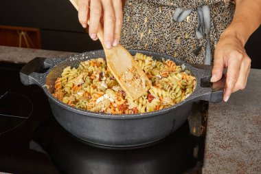 Pişmiş makarna, lezzetli bir yemek için diğer malzemelerle dolu bir kızartma tavasına boşaltılıyor..