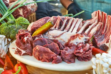 A variety of raw meat cuts, including ribs and tenderloin, displayed on a wooden board, ready for preparation and cooking. clipart